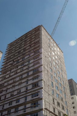 Mavi gökyüzünün arka planında yapım aşamasındaki çok katlı bir bina ve vinç.