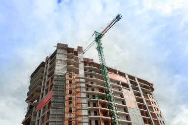 Mavi gökyüzünün arka planında yapım aşamasındaki çok katlı bir bina ve vinç.