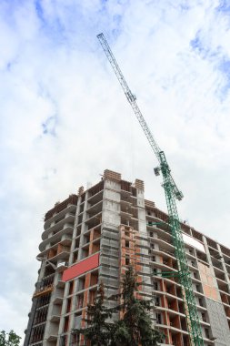 Mavi gökyüzünün arka planında yapım aşamasındaki çok katlı bir bina ve vinç.