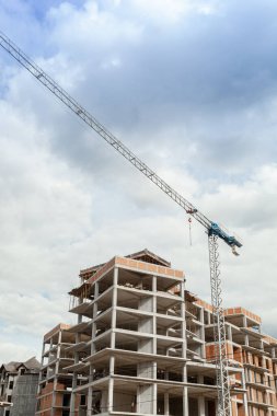 Mavi gökyüzünün arka planında yapım aşamasındaki çok katlı bir bina ve vinç.