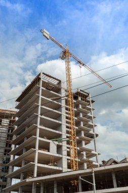 Mavi gökyüzünün arka planında yapım aşamasındaki çok katlı bir bina ve vinç.