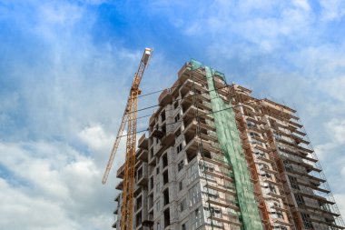 Mavi gökyüzünün arka planında yapım aşamasındaki çok katlı bir bina ve vinç.