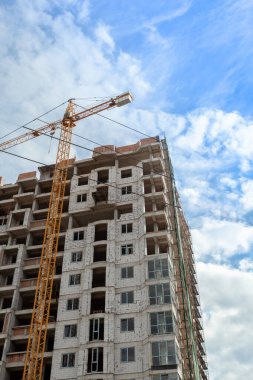 Mavi gökyüzünün arka planında yapım aşamasındaki çok katlı bir bina ve vinç.