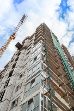 Mavi gökyüzünün arka planında yapım aşamasındaki çok katlı bir bina ve vinç.