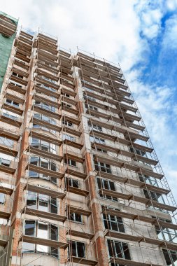 Mavi gökyüzünün arka planında yapım aşamasındaki çok katlı bir bina ve vinç.