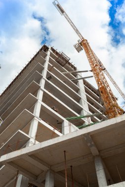Mavi gökyüzünün arka planında yapım aşamasındaki çok katlı bir bina ve vinç.