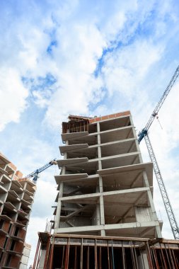 Mavi gökyüzünün arka planında yapım aşamasındaki çok katlı bir bina ve vinç.