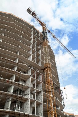 Mavi gökyüzünün arka planında yapım aşamasındaki çok katlı bir bina ve vinç.