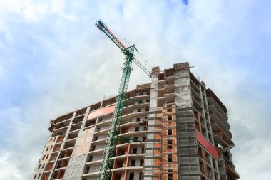Mavi gökyüzünün arka planında yapım aşamasındaki çok katlı bir bina ve vinç.