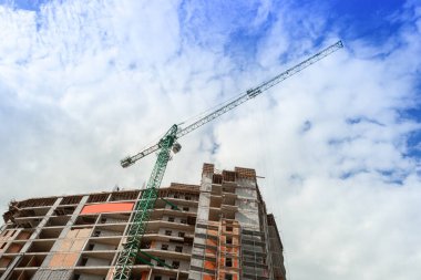 Mavi gökyüzünün arka planında yapım aşamasındaki çok katlı bir bina ve vinç.