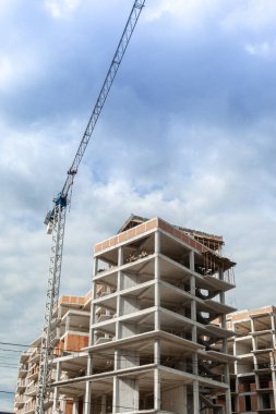 Mavi gökyüzünün arka planında yapım aşamasındaki çok katlı bir bina ve vinç.