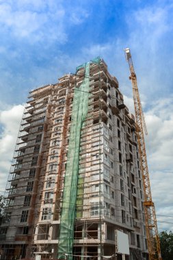 Mavi gökyüzünün arka planında yapım aşamasındaki çok katlı bir bina ve vinç.