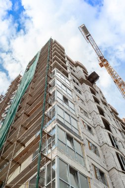 Mavi gökyüzünün arka planında yapım aşamasındaki çok katlı bir bina ve vinç.