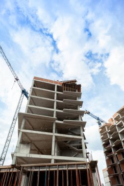 Mavi gökyüzünün arka planında yapım aşamasındaki çok katlı bir bina ve vinç.