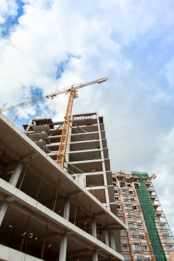 Mavi gökyüzünün arka planında yapım aşamasındaki çok katlı bir bina ve vinç.