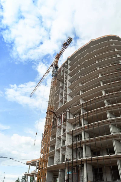 Multi-storey residential building under construction and crane on a background of blue sky