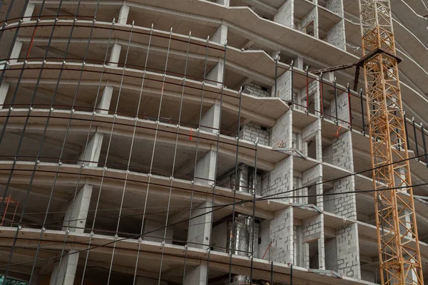 Multi-storey residential building under construction and crane on a background of blue sky