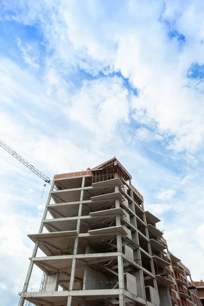 Multi-storey residential building under construction and crane on a background of blue sky