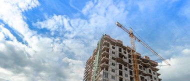 Mavi gökyüzünün arka planında inşaat halindeki çok katlı bir bina ve vinç manzarası