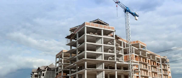 Panorama of a multi-storey residential building under construction and crane on a background of blue sky