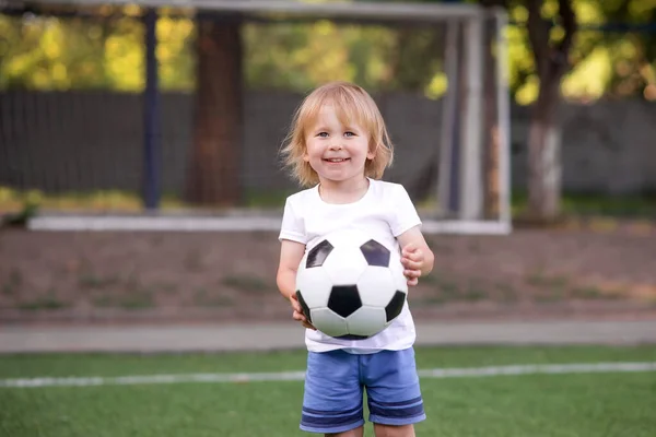 サッカー場 スタジアム に立ち ゴールポスト ネット とサッカーボールで幸せな笑顔ブロンドの幼児の少年 幼稚園や幼稚園でのサッカーレッスン 屋外活動や子供のためのスポーツの概念 — ストック写真