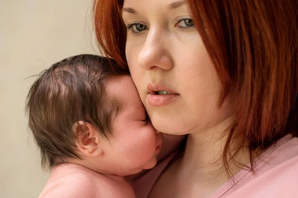 新生児の娘を抱えて真剣で心配そうな顔をした母の肖像画 幼い子供を抱えている幼い母親は目を閉じている 母と子の絆と妊産婦の問題の概念 ストック画像
