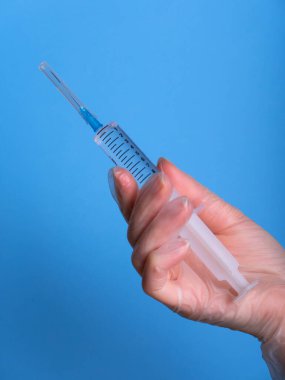 Eldeki şırınga maviye izole edildi. Bir kadın (hemşire, bilim adamı) laboratuarda kimyasallar için kırmızı, pembe (morumsu) sıvı içeren plastik şırıngayı (tek kullanımlık şırınga) elinde tutar.