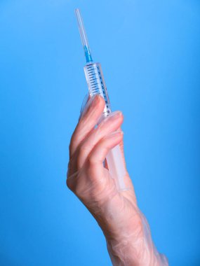 Eldeki şırınga maviye izole edildi. Bir kadın (hemşire, bilim adamı) laboratuarda kimyasallar için kırmızı, pembe (morumsu) sıvı içeren plastik şırıngayı (tek kullanımlık şırınga) elinde tutar.