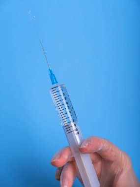 Eldeki şırınga maviye izole edildi. Bir kadın (hemşire, bilim adamı) laboratuarda kimyasallar için kırmızı, pembe (morumsu) sıvı içeren plastik şırıngayı (tek kullanımlık şırınga) elinde tutar.