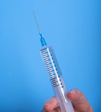 Eldeki şırınga maviye izole edildi. Bir kadın (hemşire, bilim adamı) laboratuarda kimyasallar için kırmızı, pembe (morumsu) sıvı içeren plastik şırıngayı (tek kullanımlık şırınga) elinde tutar.