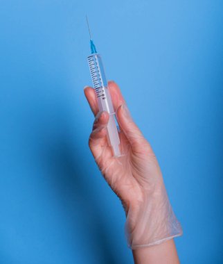 Eldeki şırınga maviye izole edildi. Bir kadın (hemşire, bilim adamı) laboratuarda kimyasallar için kırmızı, pembe (morumsu) sıvı içeren plastik şırıngayı (tek kullanımlık şırınga) elinde tutar.