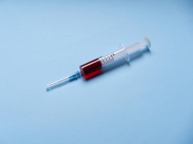 Mavi arka plan izolasyonuna şırınga. Bir ışığa karşı kırmızı sıvı içeren şırınganın yakın çekimi. 