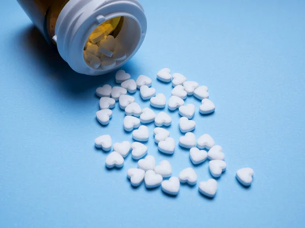 bottle of pills/ bottle of tablets for heart . Small white love pills with a plastic bottle on red colorful table. Concept of love pills, potency, loneliness, heart disease. heart pills on red background