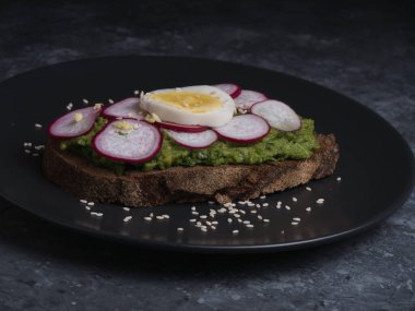 Avokado sandviçi üzerine koyu çavdar ekmeği. Ispanaklı taze avokado, guacamole, roka manzaralı. Sağlıklı kahvaltı kavramı. Sağlıklı ev yapımı Avokado tostu.