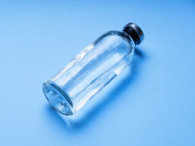 Şırınga enjeksiyonlu cam ilaç şişesi, mavi arka plan izolasyonunda damlatma sistemi. İçinde mavi sıvı bulunan bir şırınga bulunan bir infüzyon sistemini ışığa karşı yakın çekim.