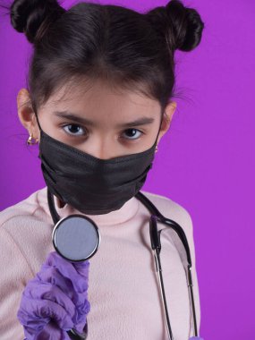 Siyah maskeli ve mor arka planda steteskobu olan tatlı bir kız. Covid-19 'u durdurun. Evde kal. Konsept. Koruyucu tıbbi maskeli genç bir kız. Karantinaya alın. Coronavirus. Kişisel tecrit.