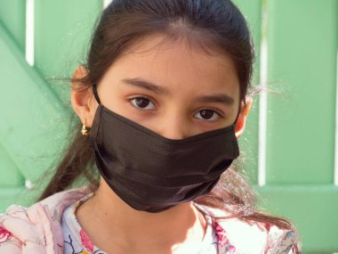 Tıbbi maskeli bir kız. Karantinaya alın. Covid-19. Yalıtım. Coronavirus kilitlenirken evinin yakınında duran tatlı küçük kız. Üzgün çocuk yalnız zaman geçiriyor, çocuk kendini yalnız hissediyor. yalnızlık