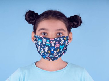 Renkli maskeli komik kız. Heyecan ve cazibe konsepti. Portreyi kapat. Stüdyo görüntüsü mavi arkaplanda. Aptalca somurtmalar komik çılgın jestler. Komik bir ifade. Covid-19. Küçük doktor. Evde kal. Kendine dikkat et.