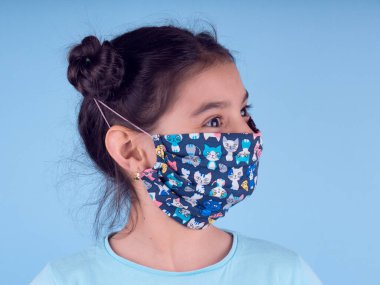 Sarı arka planda renkli maskeli şirin bir kız. Covid-19 'u durdurun. Evde kal. Karantinaya alın. Coronavirus. Kız doktoru oynuyor. Eğitim ve işgal konsepti. Kendinde kal. Alan arkaplanını kopyala