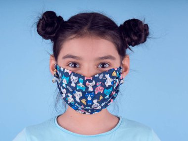 Renkli maskeli komik kız. Heyecan ve cazibe konsepti. Portreyi kapat. Stüdyo görüntüsü mavi arkaplanda. Aptalca somurtmalar komik çılgın jestler. Komik bir ifade. Covid-19. Küçük doktor. Evde kal. Kendine dikkat et.