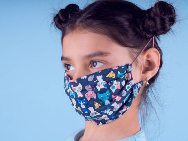 Renkli maskeli komik kız. Heyecan ve cazibe konsepti. Portreyi kapat. Stüdyo görüntüsü mavi arkaplanda. Aptalca somurtmalar komik çılgın jestler. Komik bir ifade. Covid-19. Küçük doktor. Evde kal. Kendine dikkat et.