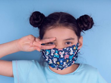 Renkli maskeli komik kız. Heyecan ve cazibe konsepti. Portreyi kapat. Stüdyo görüntüsü mavi arkaplanda. Aptalca somurtmalar komik çılgın jestler. Komik bir ifade. Covid-19. Küçük doktor. Evde kal. Kendine dikkat et.