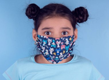 Renkli maskeli komik kız. Heyecan ve cazibe konsepti. Portreyi kapat. Stüdyo görüntüsü mavi arkaplanda. Aptalca somurtmalar komik çılgın jestler. Komik bir ifade. Covid-19. Küçük doktor. Evde kal. Kendine dikkat et.