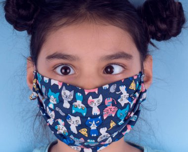 Renkli maskeli komik kız. Heyecan ve cazibe konsepti. Portreyi kapat. Stüdyo görüntüsü mavi arkaplanda. Aptalca somurtmalar komik çılgın jestler. Komik bir ifade. Covid-19. Küçük doktor. Evde kal. Kendine dikkat et.