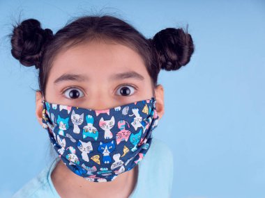 Renkli maskeli komik kız. Heyecan ve cazibe konsepti. Portreyi kapat. Stüdyo görüntüsü mavi arkaplanda. Aptalca somurtmalar komik çılgın jestler. Komik bir ifade. Covid-19. Küçük doktor. Evde kal. Kendine dikkat et.