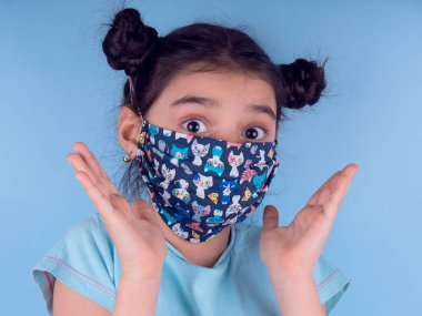 Renkli maskeli komik kız. Heyecan ve cazibe konsepti. Portreyi kapat. Stüdyo görüntüsü mavi arkaplanda. Aptalca somurtmalar komik çılgın jestler. Komik bir ifade. Covid-19. Küçük doktor. Evde kal. Kendine dikkat et.