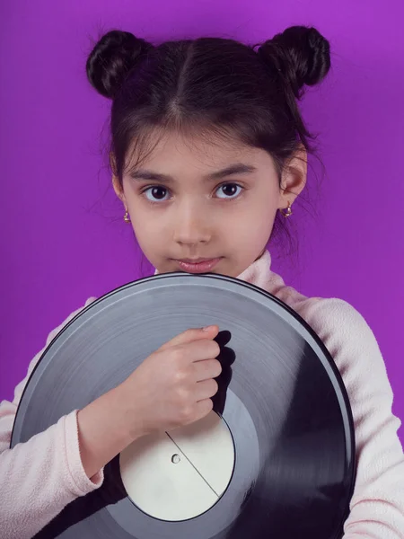 Little girl holding a vinyl record  Hiding Face. Colorful photo of a beautiful child holding a  vinyl record in her hands on purple background