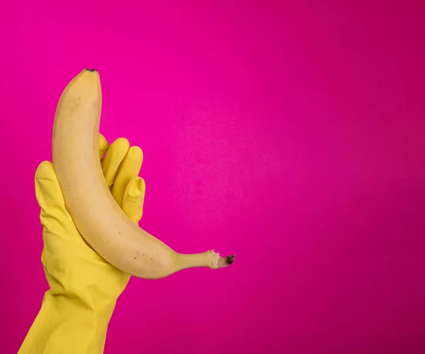 Women Hand with color rubber gloves holding  banana on color background