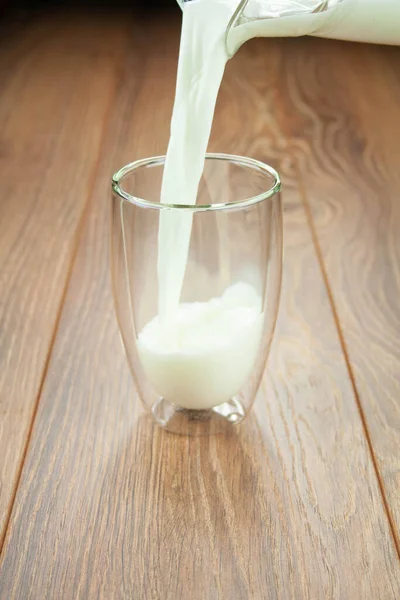 Υγιές πρωινό γάλα από κανάτα σε ποτήρι σε ξύλινο τραπέζι πιτσιλιές γάλακτος. — Φωτογραφία Αρχείου