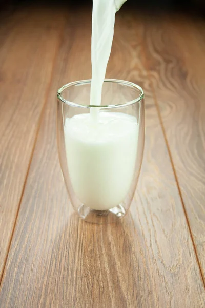 Eiwitontbijt melk uit een kan in een glas op een houten tafel spatten melk. — Stockfoto